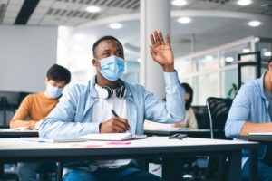 Student wearing mask in classroom raising hand